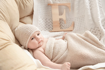 Fototapeta na wymiar Cute baby with letter E lying on soft blanket in armchair. Choosing name concept