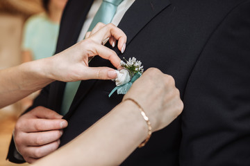 Woman pinning the boutonniere on the groom's jacket. Close up picture. Unrecognizable man....