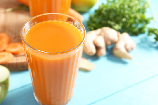 Glass of fresh carrot juice on color wooden background
