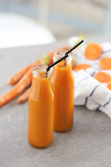 Bottles of fresh carrot juice on grey table