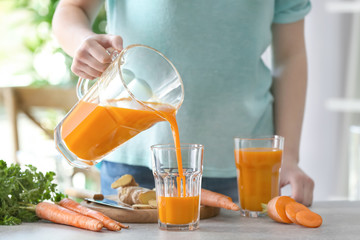 Young woman filling glass of fresh carrot juice in the kitchen