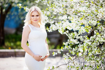 Portrait of beautiful pregnant woman in the flowering park. Young happy pregnant woman enjoying life in nature.