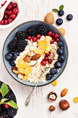 Healthy classic breakfast with oatmeal, cornflakes and various fresh berries on a white wooden surface.