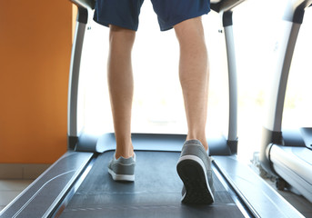 Fototapeta premium Sporty young man training legs on treadmill in gym, closeup