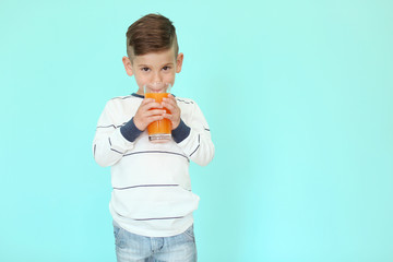 Cute little boy drinking juice on color background