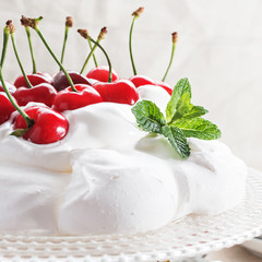Pavlova - meringue cake with  fresh cherries  on  glass cake stand on marble background, copy space, close up, selective focus.