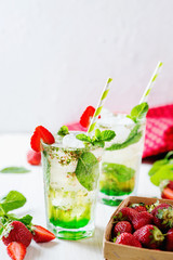 Alcoholic and non-alcoholic refreshing drinks, cold sparkling cocktail with ice, green mint and fresh strawberries in a beautiful glass on a light background 