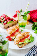 Breakfast, business lunch, sandwiches croissant with ham, cheese, sauce, lettuce, tomato and strawberry mint ice-cold cocktail on a light background 