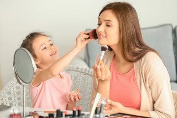 Young woman and her little daughter applying makeup at home