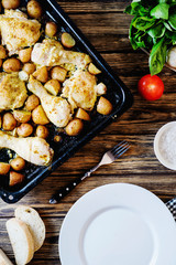 Hearty and delicious dinner, baked chicken legs and thighs with potatoes, onions, tomatoes, spices, herbs and white bread on a dark wooden background