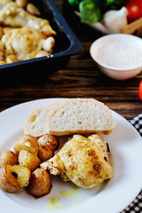 Hearty and delicious dinner, baked chicken legs and thighs with potatoes, onions, tomatoes, spices, herbs and white bread on a dark wooden background