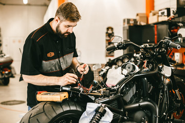 Confident young man repairing motorcycle in repair shop - electronics repair. This bike will be perfect.