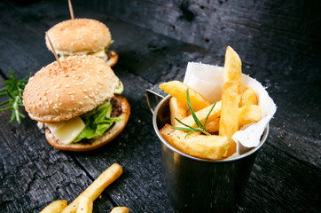 Hamburger with french fries on a burnt, black wooden table. Fast food meal. Homemade hamburger consist of beef meat, lettuce, tomato, bins, dressing, cheese and spices. Vintage 
