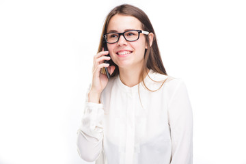 Beautiful young girl in a white shirt on white isolated background talking on a mobile phone. Smiles, portrait to the waist