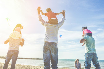 Families with children flying with kites on the beach at sunset - Adult friends playing with son and daughters on summer vacation - Holidays concept - Focus on left people - Retro filter