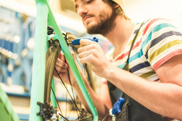 Bearded bicycle mechanic doing his professional work in workshop - Young man checking new carbon wheel superbike indoor - Repairing bikes concept -  Focus on left hand fingers - Retro filter