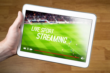 Man watching live sport stream online with mobile device. Hand holding tablet with imaginary video player and streaming service. © terovesalainen