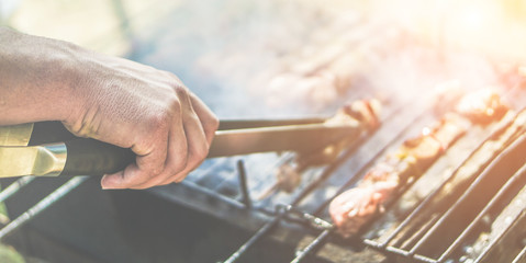 Young man cooking meat on barbecue at home in backyard - Chef putting some meat skewers on grill in park outdoor - Summer, food concept - Focus on center hand - Vintage retro filter