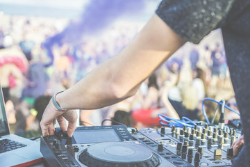 Dj mixing at disco party on the beach outdoor - Disc jockey playing music with smoke bombs colors and people dancing in background - Festival, fun concept - Focus on left hand - Warm vintagefilter
