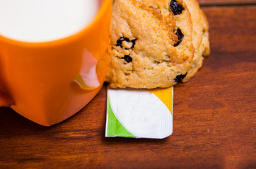 Close up of an orange glass of milk with a chocolate cookie baked with stevia, with a stevia paper...