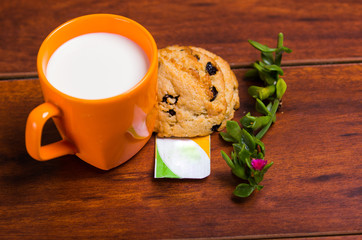 An orange glass of milk with a chocolate cookie baked with stevia, with a stevia paper bag and a branch of stevia plant, on wooden background