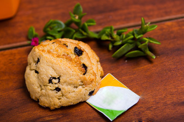 Close up of a chocolate cookie baked with stevia, with a stevia paper bag and a branch of stevia plant, on wooden background