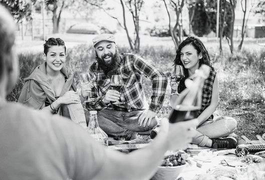 Happy friends making picnic on city park outdoor - Young hipster people drinking wine and laughing outside - Main focus on bearded man - Black and white editing - Contrast filter