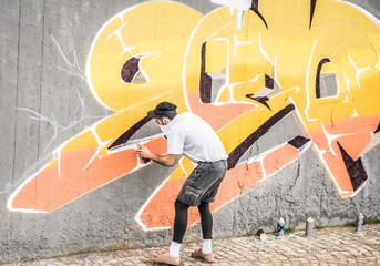 Graffiti artist covering his face while painting with color spray on the wall - Urban , street art concept - Focus on his head - Warm contrast filter