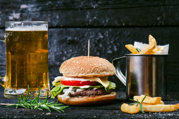 Hamburger with french fries, beer on a burnt, black wooden table. Fast food meal. Homemade...