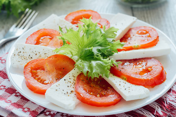 Feta cheese slices with tomato on white plate 