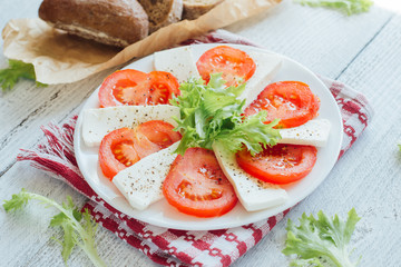 Feta cheese slices with tomato on white plate  