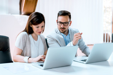Young businessman discussing with his female colleague, and using a lap top in the office.