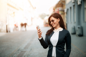 Smiling girl texting on the smart phone while walking in the street.