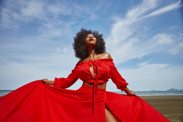 Female dark skin model with curly hair in red dress enjoing at the sea coast