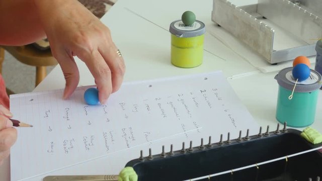 Artiest writes down her ideas for matching bead colors togeather on paper in her studio