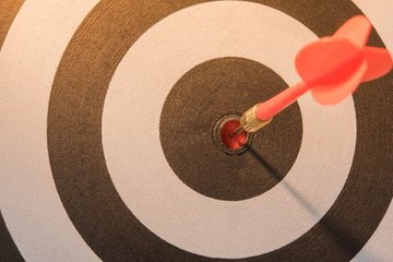 Red dart target arrow hitting on bullseye with sun light