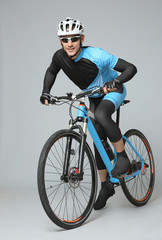 Obraz na płótnie Canvas Young sporty cyclist riding bicycle on grey background