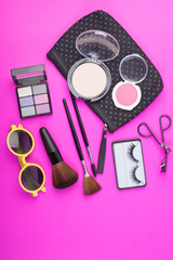 Fototapeta premium Top view of a make up bag, with cosmetic beauty products spilling out onto a pink background.