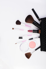 Top view of a make up bag, with cosmetic beauty products spilling out onto a white background.