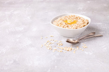 Porridge with oil in a bowl on a gray concrete background. Healthy useful breakfast. Selective focus. Copy space