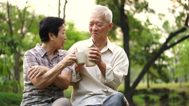 Asian senior couple showing affectionate and care through a cup of coffee in morning bright natural park