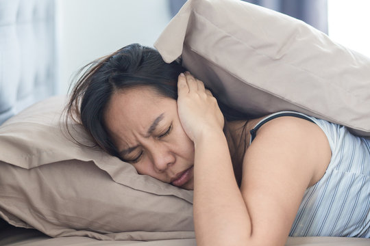 Young woman lying in bed suffering from sound covering head and ears with pillow making unpleasant face. early wake up not getting enough sleep