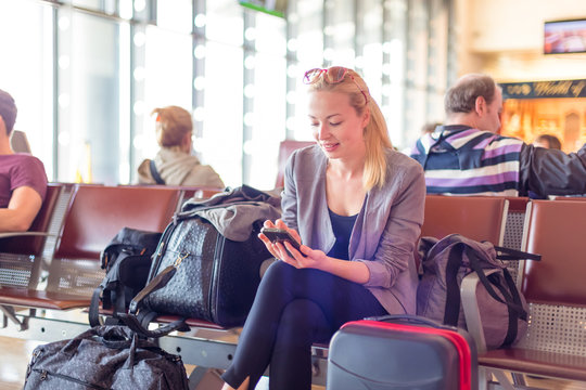 Casual blond young woman using her cell phone while waiting to board a plane at the departure gates. Wireless network hotspot enabling people to access internet conection. Public transport.