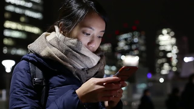 Young Asian Woman texting cellphone at night on city street