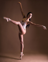 Fototapeta premium beautiful woman ballet dancer posing on toes over beige