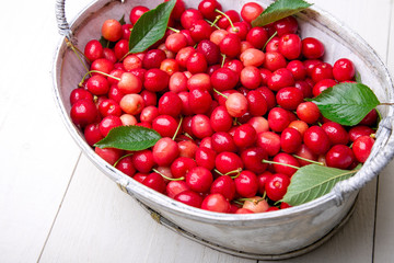 Red cherries in white basket on white wooden background. Cherry close up.