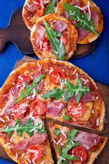 Homemade pizza with prosciutto, tomato, arugula on wooden board blue background. Top view.