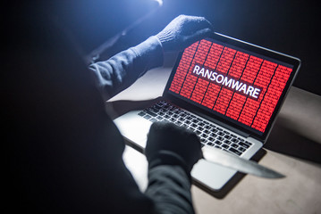 Male hacker threading computer laptop with knife showing on screen with ransomware warning, internet security system concept