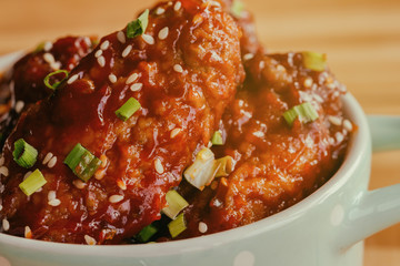 Korean fried chicken wings sprinkled with sesame and spring-onion on wood plate. Korean barbecue chicken wing delicious,moist and spicy. Close up on fried chicken wings in Korean style on wood table.