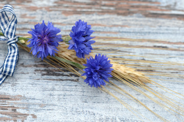 Cereal ears with cornflowers lying on wood